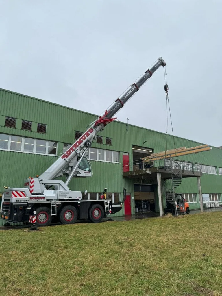 Mobilkran hebt Maschinenteile in das Produktionsgebäude von priomold in Schömberg zur Modernisierung und Erweiterung des Maschinenparks.