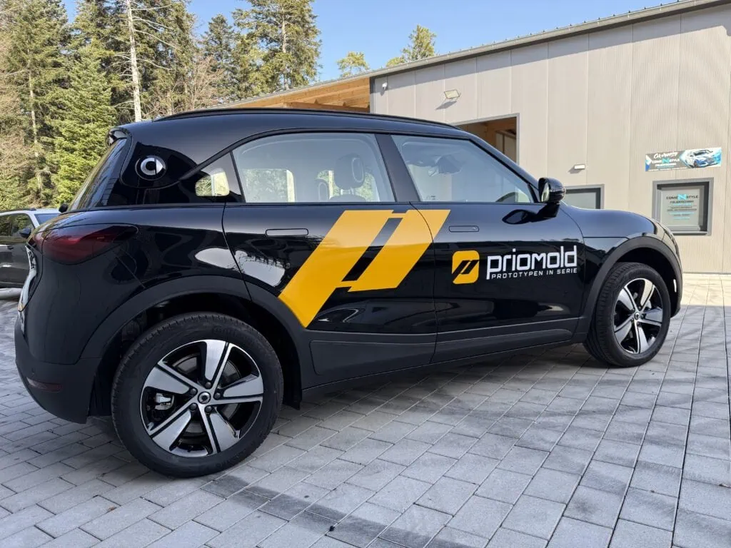 Gebrandeter Smart der priomold E-Flotte vor dem Unternehmensgebäude als Symbol für Elektromobilität und nachhaltige Mobilität im Unternehmen.