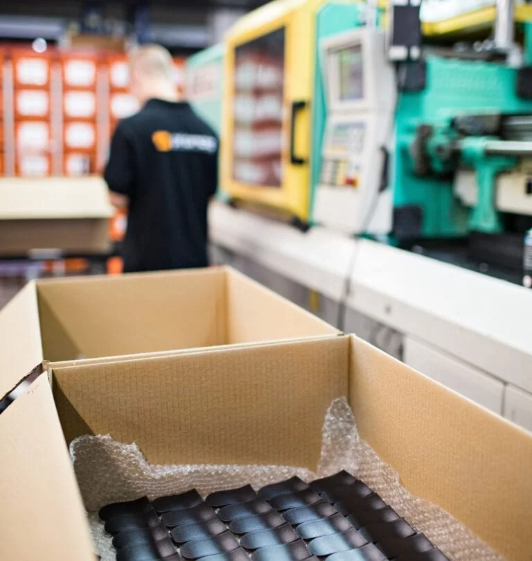 Verpackte schwarze Spritzgussteile vor einer Spritzgussmaschine bei priomold